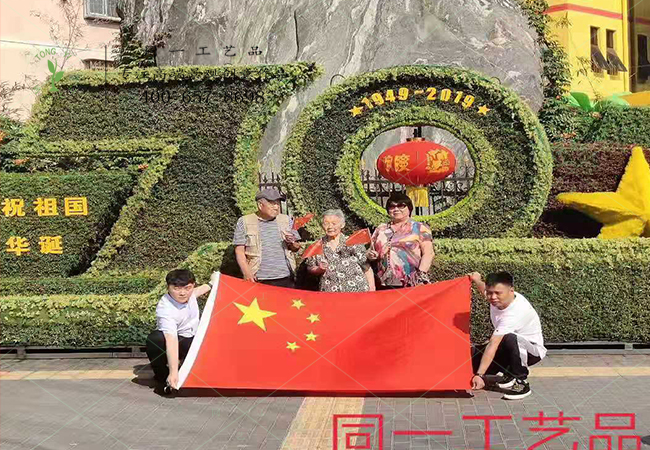 北京游客在植物綠雕國慶綠雕前舉國旗合影
